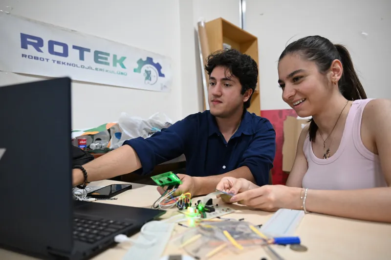 MCBÜ Robot Teknolojileri Kulübünde dizüstü bilgisayar ve elektronik kartlarla robot programlayan iki öğrenci
